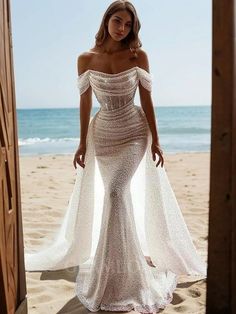 a woman standing on top of a beach next to the ocean wearing a white dress