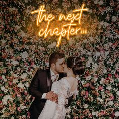 a newly married couple kissing in front of a flower wall with the words, the next chapter