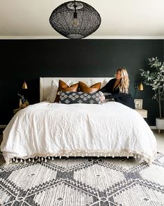 a woman sitting on top of a bed next to a black and white rug in a bedroom