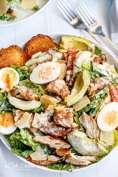 a salad with hard boiled eggs and chicken in it on a white plate next to silverware