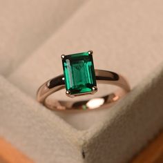 an emerald colored ring sits in a box