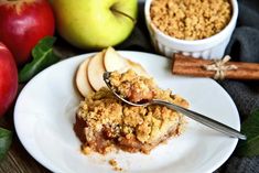 a white plate topped with an apple crumb cake next to apples and cinnamon sticks