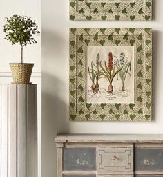 two paintings hanging on the wall next to an old dresser and vase with flowers in it