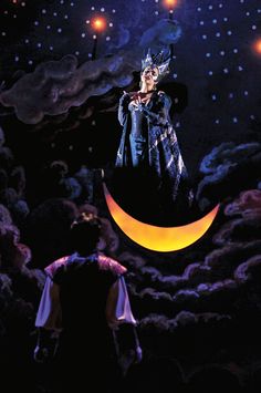 a man standing on top of a moon next to another man in the sky with lights