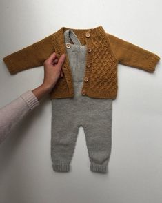 a person holding onto a baby's knitted sweater and pant suit with buttons