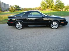 a black sports car parked on the side of a road in front of some grass