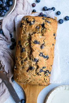 a loaf of blueberry bread sitting on top of a wooden cutting board next to a bowl of blueberries