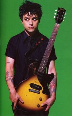 a man holding an electric guitar in front of a green background