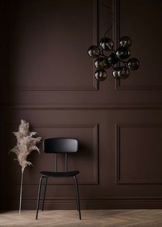 a black chair sitting in front of a brown wall with a chandelier hanging from it