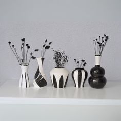 five black and white vases are lined up on a shelf with flowers in them