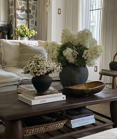 a coffee table with flowers and books on it in front of a couches window