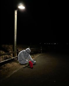 a man sitting on the side of a road next to a street light at night