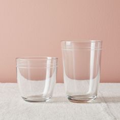 two clear glass cups sitting on top of a white tablecloth covered table next to a pink wall