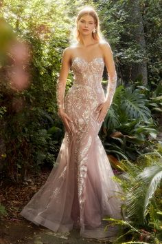 a woman in a wedding dress standing on a path surrounded by trees and bushes with her hands on her hips