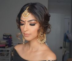 a woman with dark hair wearing gold jewelry and black makeup looks off to the side