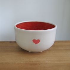 a white bowl with a red heart painted on the side sitting on a wooden table