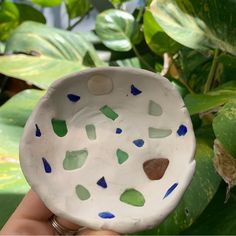 a hand holding a white bowl with blue and green sea glass pieces in the center