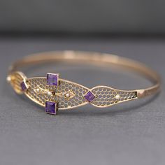 This pretty, lacy bangle is truly one of a kind. The center of the bracelet features two square cut bezel set amethysts, each about 0.33ct. They are matched by two smaller square amethysts set on point, each weighing approximately 0.10ct. Five seed pearls accent the bracelet but perhaps the main focus is the super intricate honeycomb structure of the top of the bangle. The bangle is nearly round and measures 2.5" across in diameter and is 2 3/8" tall inside. Across the top the bracelet measures Amethyst Bridal Jewelry, Elegant Purple Bracelets For Wedding, Elegant Purple Wedding Bracelets, Rectangular Fine Jewelry Wedding Bracelet, Elegant Amethyst Bangle Bracelet, Elegant Amethyst Bracelets For Wedding, Luxury Purple Bracelets For Wedding, Amethyst Bracelet For Weddings, Purple Gemstone Bangle For Formal Occasions