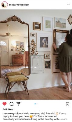 a woman standing in front of a mirror looking at pictures on the wall