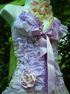 a dress made out of purple and white lace with flowers on the side, attached to a mannequin