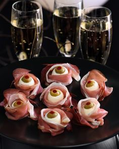 ham and cheese appetizers on a black plate with glasses of champagne in the background