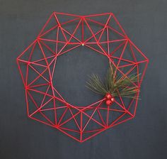 a red wire wreath with pine branches and berries on it against a black background,