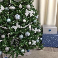 a decorated christmas tree with blue and silver ornaments on it, next to a gift box