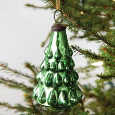 a green glass christmas tree ornament hanging from a pine tree