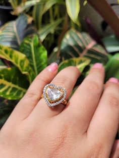 a woman's hand with a diamond ring on it and green plants in the background