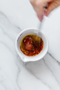 a person is dipping sauce into a white bowl on a marble counter top with a spoon in it