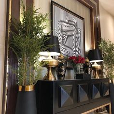 a black and gold sideboard with two lamps on top, plants in vases next to it