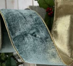 a roll of blue and gold velvet ribbon on a wooden fence with holly leaves in the background