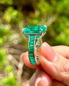 a person holding a ring with an emerald stone in it's center and green grass behind them