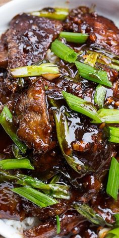 a white plate topped with meat covered in sauce and green onions on top of rice