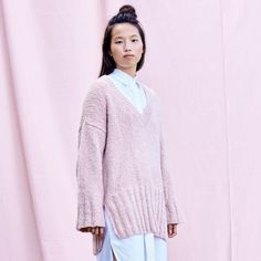 a woman standing in front of a pink backdrop wearing a sweater and skirt with high slits