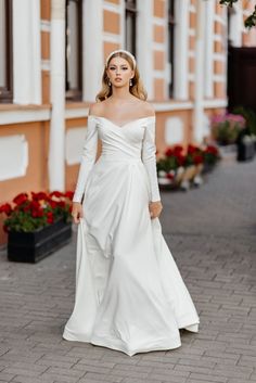 a woman in a white wedding dress is standing on the street with flowers behind her