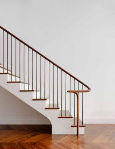 a white staircase with wooden handrails and hardwood flooring in an empty room