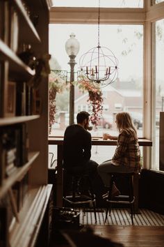 a man and woman sitting at a table in front of a large window looking out onto the street