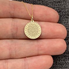 a hand holding a gold necklace with an image of a coin on the front and side