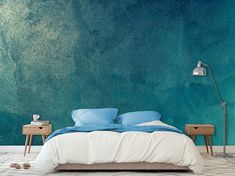 a bed with blue sheets and pillows in front of a green wall