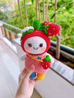 a hand holding a small crocheted doll with a strawberry on it's head