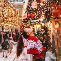 a woman standing in front of a christmas tree looking up at the sky with her eyes closed