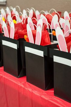 small bags with bunny ears are lined up on a red tablecloth for an event