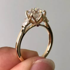 a close up of a person's hand holding a gold ring with two diamonds