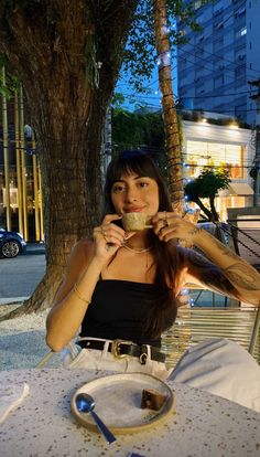 a woman sitting at an outdoor table drinking from a cup