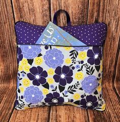 a purple and yellow flowered pillow with polka dots on the bottom, sitting on a wooden surface