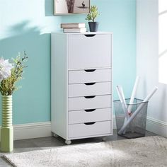 a white cabinet with five drawers in a blue room next to a vase and flowers