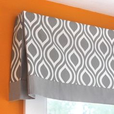 a window with a gray and white valance hanging from it's side next to an orange wall