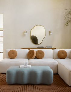 a living room with a large white couch and wooden coffee table in front of a round mirror