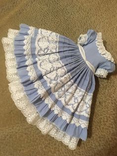 a blue and white dress with lacy trims on the bottom, sitting on a brown carpet